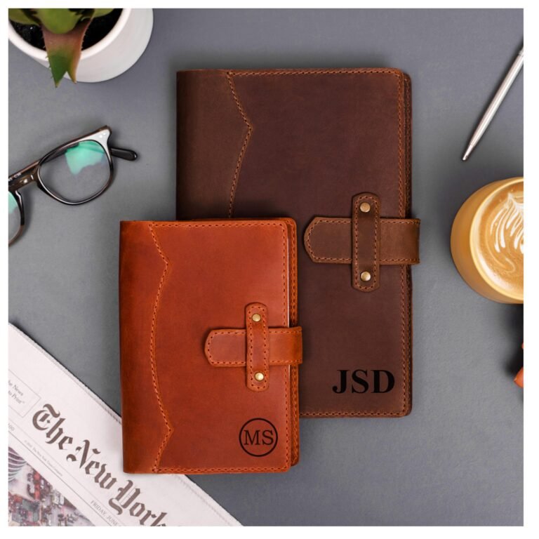 Two leather journals, one with initials, on a gray surface with accessories